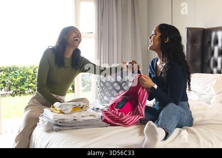 Ridendo diverse amiche, lavatrice pieghevole sul letto in camera da letto, con cestino in plastica Foto Stock