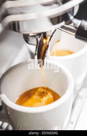 Primo piano dell'espresso appena estratto con crema ricca versata in tazze bianche dal supporto Foto Stock