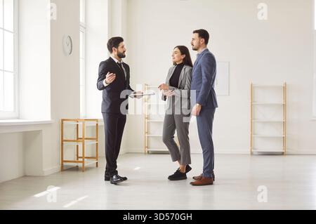 Agente immobiliare professionale che mostra l'appartamento a giovani coppie e spiega le caratteristiche durante il tour della proprietà. Foto Stock
