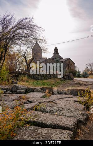 Un'antica lapide con sullo sfondo una chiesa armena del monastero Saghmosavanq. La chiesa è vecchia e il muro di pietra è fatto di grandi rocce. Il Foto Stock