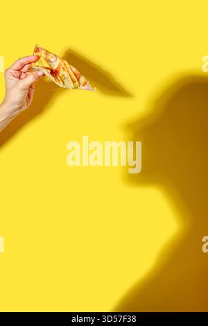 una fetta di pizza in mano su sfondo giallo con ombre Foto Stock