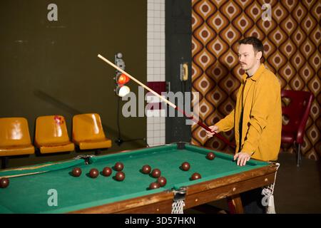 L'uomo gioca a biliardo in una stanza in stile retrò con pareti a righe Foto Stock