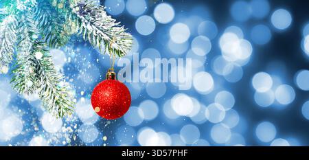 Palla di Natale appesa al ramo dell'abete su luci sfocate su sfondo blu. Design banner Foto Stock