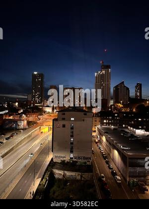 Una vibrante vista notturna di Leeds, Inghilterra, caratterizzata da alti edifici illuminati, una strada trafficata e un cielo blu profondo. Catturato dall'alto Foto Stock