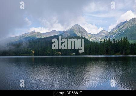 Le vette ricoperte di foreste si riflettono sul lago Štrbské pleso, mentre una nuvola di nebbia e nebbia si stabilirono sul paesaggio. Foto Stock