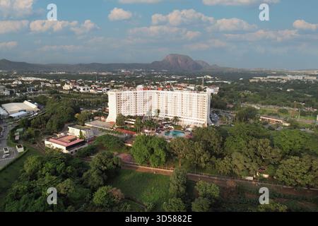 Vista aerea di un complesso alberghiero immerso nel verde lussureggiante, con la montagna di Aso Rock in lontananza sentinella, Abuja, Nigeria. Foto Stock