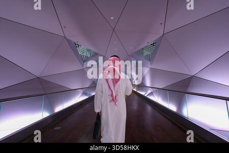 Uomo saudita che cammina attraverso la passerella della KAFD a Riyadh, Arabia Saudita, visto da dietro, diretto a lavorare nel moderno quartiere degli affari. Uso editoriale o Foto Stock