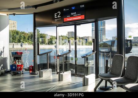 25 agosto 2025, Mosca, Russia. Il terminal dei trasporti presenta cancelli automatici, aree con posti a sedere e una vista panoramica sul fiume con edifici sotto a. Foto Stock