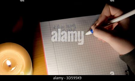 Lavorare su problemi di matematica in solitudine tranquilla accanto a una candela luminosa. Foto Stock