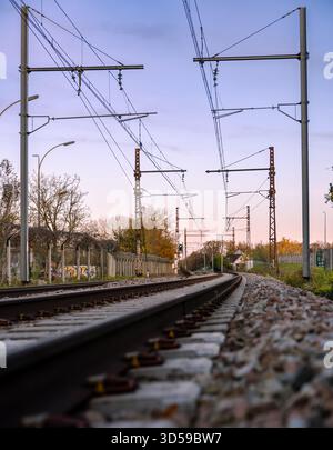Francia.i binari ferroviari si estendono in lontananza, incorniciati da fogliame autunnale e da alti piloni catenari. Cavi e lampioni pendono sopra i binari. Foto Stock