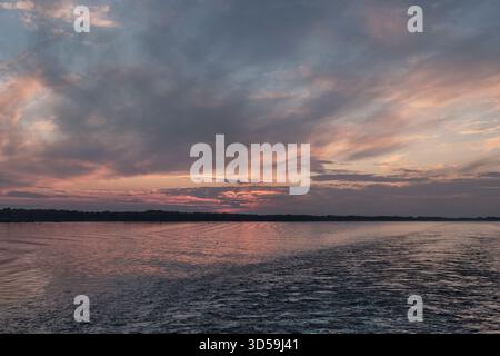 Tramonto spettacolare sull'ampio fiume Volga. Cielo pieno di nuvole di grigio scuro e rosa tenue, i loro colori si riflettono intensamente sulla superficie dell'acqua, con dist Foto Stock