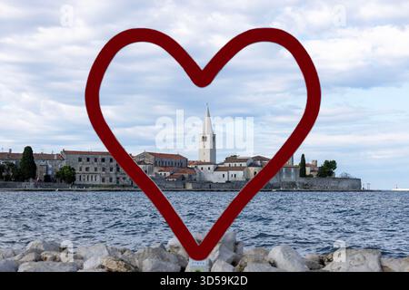 Porec, Croazia, Istria - 25 settembre 2023: Vista dalla spiaggia dal cuore rosso Parenzo della città con il campanile della Basilica di Eufrrasio Foto Stock