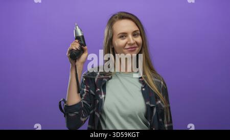Donna che tiene un trapano di potere con sicurezza davanti a un vivace sfondo viola, che mostra indipendenza, empowerment e moderno spirito fai da te. Foto Stock