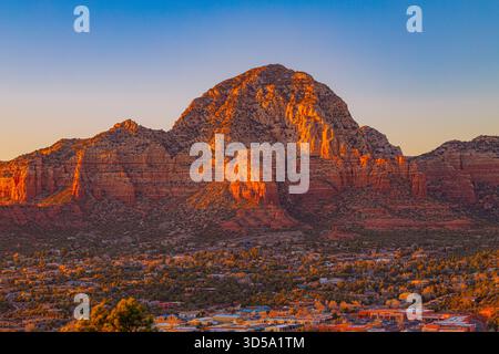 Un caldo tramonto illumina le iconiche formazioni di roccia rossa di Sedona, Arizona. Le scogliere scintillanti si innalzano sopra la città, creando un paesaggio suggestivo Foto Stock
