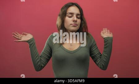 La giovane donna ispanica con collana a cuore solleva entrambe le mani con un gesto arrugginito in uno studio rosa; rassegnazione. Foto Stock