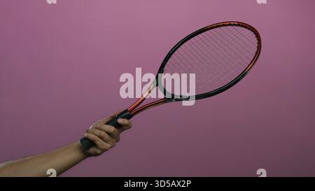 Uomo che tiene la racchetta da tennis contro il muro rosa mostrando una mano isolata e attrezzature sportive in una posizione impressionante. Foto Stock