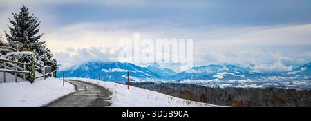 La strada tortuosa attraverso la neve fresca conduce ad una vista panoramica delle Alpi svizzere e della valle ad Aeugst am Albis, Svizzera Foto Stock
