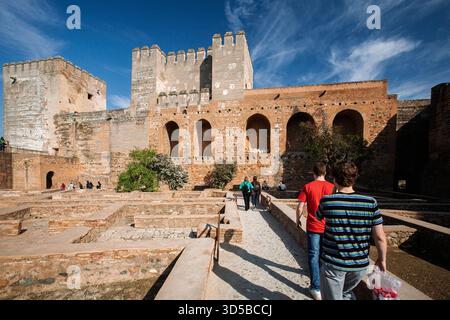 I visitatori passeggeranno davanti alle antiche mura di mattoni e alle torri dell'Alcazaba nell'Alhambra, godendosi il sito storico in una giornata di sole a Granada. Foto Stock
