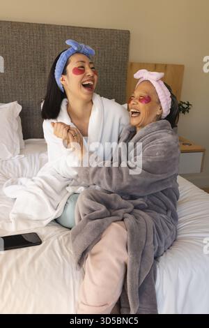Una famiglia asiatica che ride seduto insieme sul letto in una camera da letto con luce soffusa, con toppe sotto gli occhi rosa Foto Stock