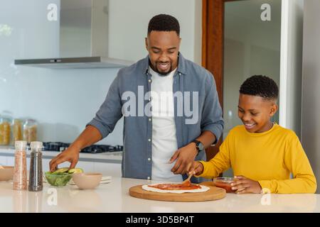 In cucina, padre e figlio preparano pizza fatta in casa, trascorrendo del tempo insieme Foto Stock