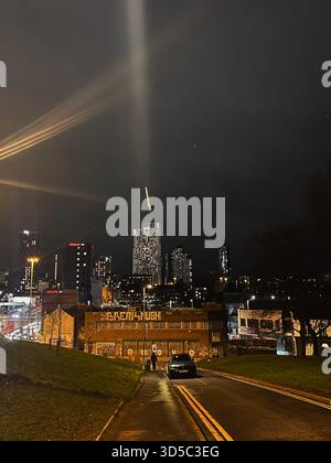 Spettacolare vista notturna dello skyline di Leeds con moderni grattacieli e fasci di luce nel cielo nuvoloso. Paesaggio urbano notturno in Inghilterra con edifici illuminati Foto Stock