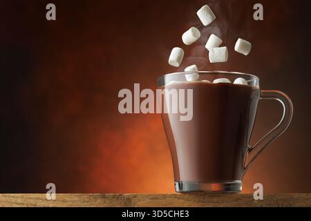 Marshmallow che cadono nella tazza per la cottura a vapore di cioccolata calda su sfondo marrone Foto Stock