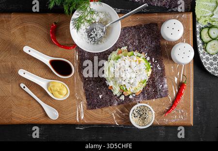 Il processo di creazione di un creativo sushi hamburger con salmone, uova fritte, formaggio, cetrioli e avocado su uno sfondo testurizzato. Fase 8. Vista dall'alto Foto Stock