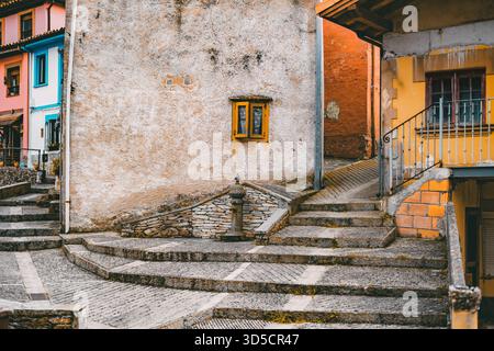 Vicolo rustico colorato a Cudillero con pareti testurizzate, gradini in pietra, una piccola fontana e vivaci cornici delle finestre, che catturano l'affascinante vill mediterranea Foto Stock