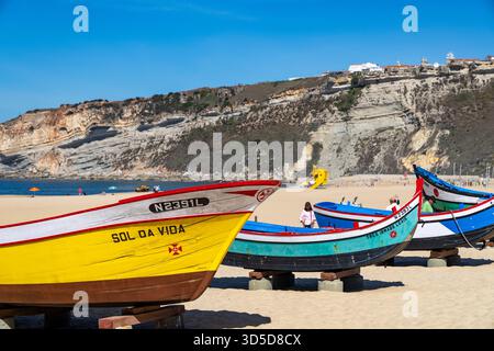 Spiaggia di Nazare, costa argentata del Portogallo, mostra di barche da pesca tradizionali portoghesi storiche multicolore sulla spiaggia, Portogallo, Europa Foto Stock