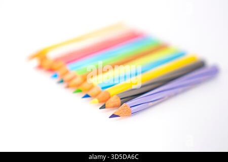 Una fila colorata di matite da disegno su uno sfondo bianco pulito con una profondità di campo ridotta, concentrata sui puntali. Foto Stock