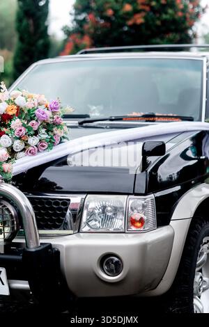 Vista ravvicinata del cappuccio di un SUV nero decorato per un matrimonio con un bouquet floreale colorato e un nastro in raso bianco. Foto Stock