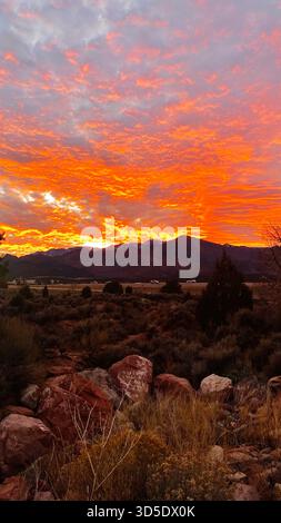 Il vivace tramonto arancione illumina una valle desertica con le rocce in primo piano e le montagne lontane nello Utah. Parco nazionale di Zion Foto Stock