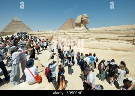 Folle di persone che visitano la sfinge e le antiche piramidi della necropoli di giza sotto il cielo limpido, il Cairo, l'Egitto Foto Stock