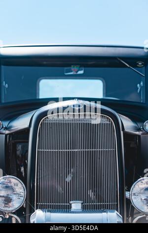 Vista frontale ravvicinata della griglia dell'automobile blu d'epoca restaurata e dell'ornamento cromato del cofano. Barre della griglia cromate verticali, parafanghi arrotondati, cornice della testa Foto Stock