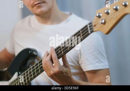 Primo piano di un uomo che suona un basso elettrico nero, concentrandosi sul posizionamento delle dita e sulla postura. Foto Stock