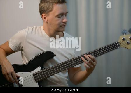Primo piano di un uomo che suona un basso elettrico nero, concentrandosi sul posizionamento delle dita e sulla postura. Foto Stock