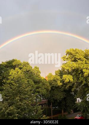 Un arcobaleno morbido e colorato si innalza su fitti alberi verdi durante una calda ora d'oro a Hull, in Inghilterra. Foto Stock