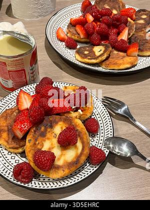 Una vista ravvicinata dei pancake fatti in casa conditi con fragole fresche su un piatto a motivi geometrici. La colazione e' allestita su un tavolo di legno, Foto Stock