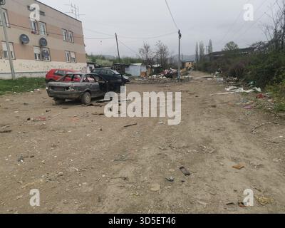 Strada secondaria polverosa con auto abbandonate e terreno disseminato Foto Stock