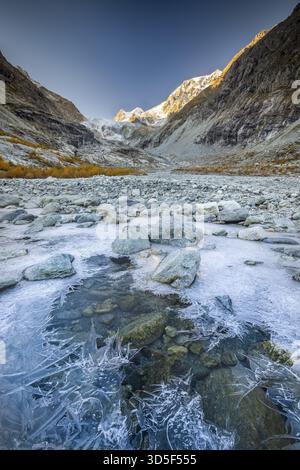 Strutture ghiacciate sul torrente di montagna con larici autunnali e panorama montano, ghiacciaio Ferpecle, Val d'Herens, Canton Vallese, Svizzera Foto Stock