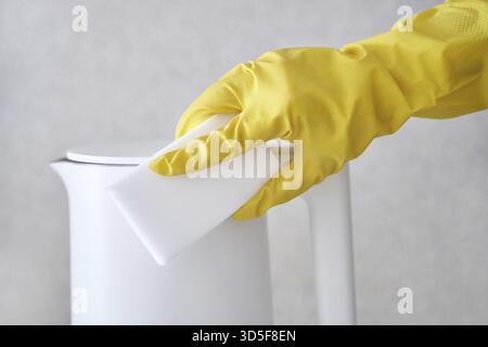 Persona che pulisce bollitore bianco con guanto giallo e spugna per la manutenzione e l'igiene della cucina Foto Stock