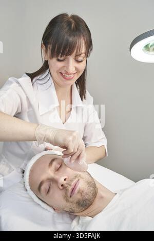 Medico che fa la routine cutanea. Trattamento di maternità in salone. Concetto di assistenza sanitaria. Uomo. Massaggio facciale pandemico con agopuntura guasha. Procedura anti-età Foto Stock