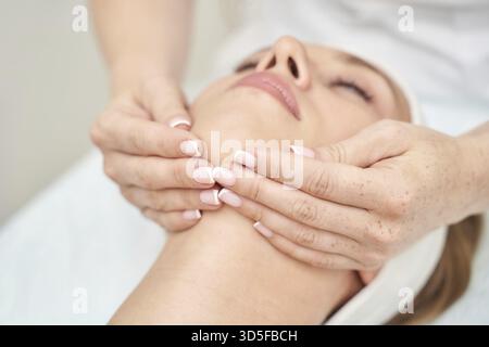 Donna caucasica che riceve un rilassante massaggio al collo presso la spa con mani delicate e luce soffusa Foto Stock
