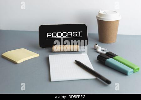 Smartphone con podcast di iscrizione, cuffie wireless, blocco note, pennarelli, tazza da caffè, concetto di formazione online Foto Stock
