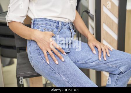 Giovane donna ispanica in jeans denim eleganti seduta su sedia nera con top bianco Foto Stock
