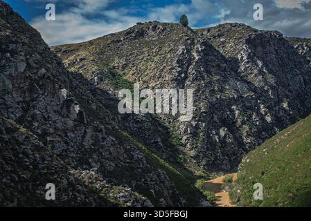 Questa immagine cattura una vista mozzafiato di una catena montuosa con una valle profonda e un cielo luminoso Foto Stock