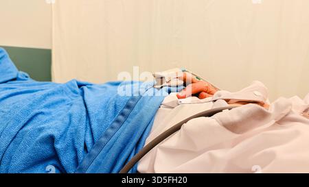 Paziente che riposa sul letto di ospedale con la mano collegata al dispositivo di monitoraggio medico durante l'esame clinico e la procedura di trattamento sanitario. Pro Foto Stock
