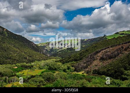 Questa vista panoramica mostra una vibrante valle circondata da colline verdeggianti e un cielo spettacolare, perfetto per gli amanti della natura Foto Stock