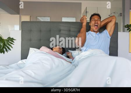 Uomo che si allunga e sbadiglia a letto mentre la donna dorme pacificamente accanto a lui Foto Stock