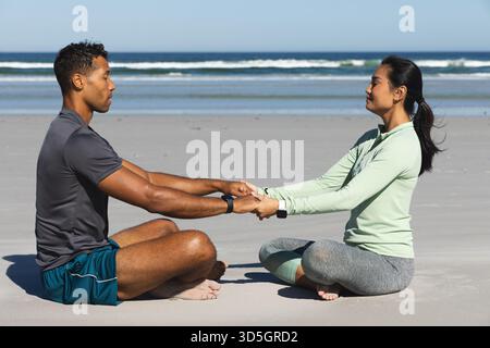Coppia seduta sulla spiaggia che si tiene per mano, godendo di una tranquilla meditazione mattutina insieme Foto Stock